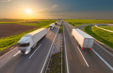 Excess Transportation Image Many delivery trucks driving through agricultural fields. Fast blurred motion image on the freeway at beautiful sunset. Freight scene on the motorway near Belgrade Serbia.