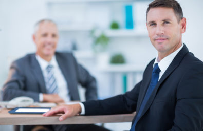 Confident businessman looking at camera with colleague behind in Confident businessman looking at camera with colleague behind in